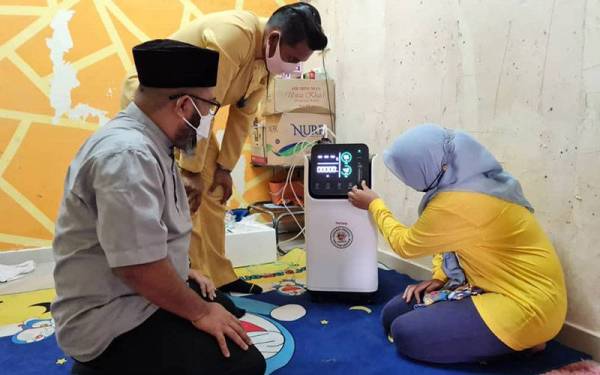 Norfardilatul Akmar (kanan) sedang mencuba alat bantuan pernafasan yang disalurkan oleh MUIP sambil diperhatikan Dr Asmadi (kiri).