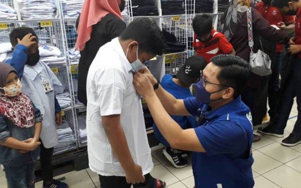 Noor Azleen memakaikan pakaian seragam sekolah dalam program Kembali ke Sekolah 2022 di pasar raya Econsave Permas.
