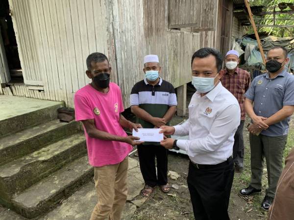 Ruji (kanan) menyampaikan bantuan berkenaan kepada Zulkifli di kediamannya di Kampung Putat 7 di sini.