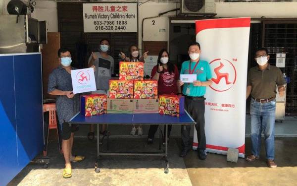 Hong (kanan) menyerahkan sumbangan wang tunai, rhadiah Tahun Baharu Cina dan Air Penyejuk Badan Cap Kaki Tiga kepada Penyelia Victory Children Home, Loh (kiri).