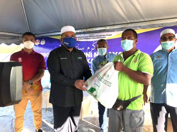 Ahmad Marzuk Shaary (dua, kiri) menyampaikan bantuan makanan kepada nelayan, Fadli Abdullah, 46, (dua, kanan) di Pasar Nelayan, Kampung Pulau Gajah, Kota Bharu pada Sabtu.