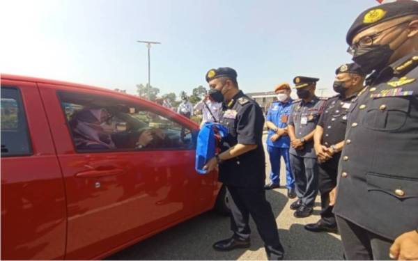 Aedy Fadly (dua, kiri) menyampaikan kit keselamatan jalan raya kepada seorang pengguna ketika melalui Dataran Melang, Kuala Pilah.