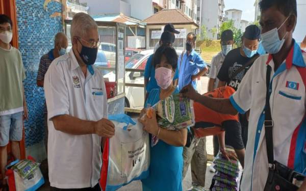 Hassan (kiri) menyerahkan sumbangan kepada penerima dalam program serahan sumbangan bakul makanan dan limau mandarin di Flat Taman Cendana pada Sabtu.