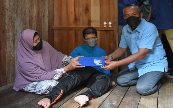 Ruslin (kanan) menyerahkan kad pengenalan kepada OKU, Hazbillah (tengah) yang ditemani ibunnya, Siti Meriam di Kampung Kubang Tepak, Manir pada Sabtu. - Foto Bernama 