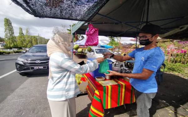 Seorang pelanggan membeli dua bungkus air kelapa muda di gerai Nur Muzammir (kanan) di Jalan Stadium di sini pada Ahad.