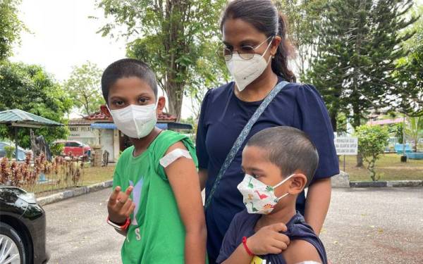Malini menemani Shivvaen (kiri) dan Dhanvinn (depan) ketika mendapatkan suntikan vaksin di PPV HPP di Dewan Sri Puteri pada Isnin.