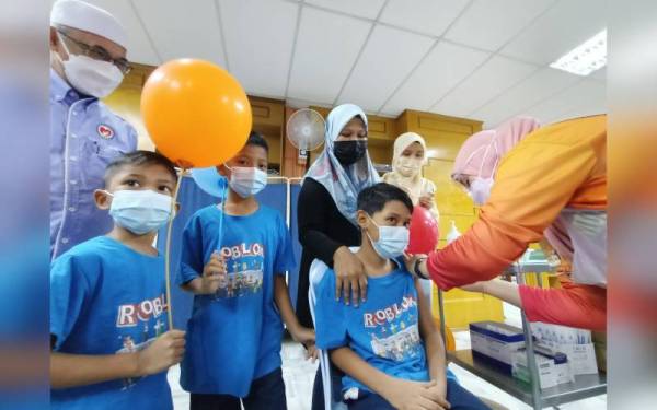 Mohamad Irfan Hakimie ditemani ibunya, Fathiyah menerima suntikan vaksin Covid-19 bersama dua adiknya, Mohamad Ikhwan Nadrin (dua dari kiri) dan Mohamad Izz Zafri.