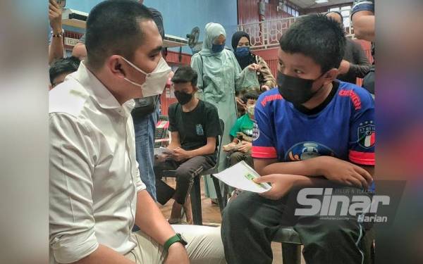 Dr Muhamad Akmal (kiri) bertanyakan sesuatu kepada seorang kanak-kanak yang menerima vaksin di PPV Dewan Datuk Ahmad Ithinin, Merlimau Pasir pada Khamis.