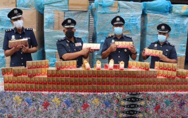 Mohd Nasir (dua dari kiri) menunjukkan rokok yang dirampas di sebuah rumah tidak bernombor di Pengkalan Chepa pada Isnin lalu.