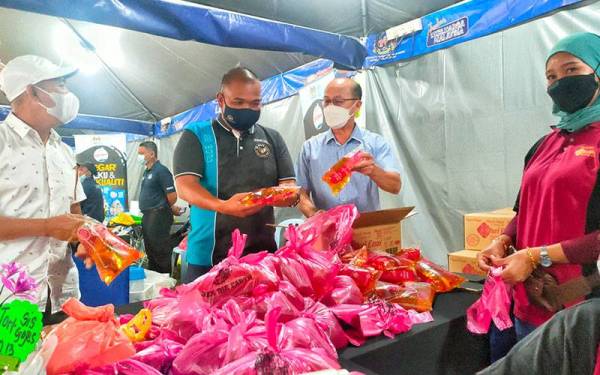 Zahari (dua dari kiri) dan Hee Sem (tiga dari kanan) melihat minyak masak peket yang dijual pemborong kepada pengunjung PJKM di Durian Tunggal, di sini, pada Sabtu.