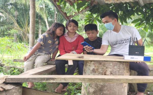 Mazlieyana (tengah) bersama sepupunya, Nuremly Khairul Azwan, 8, (kiri) dapat melayari internet di halaman rumah di Kampung Labi, selepas WiFi disediakan di rumah mereka oleh Adrian Edy (kanan).