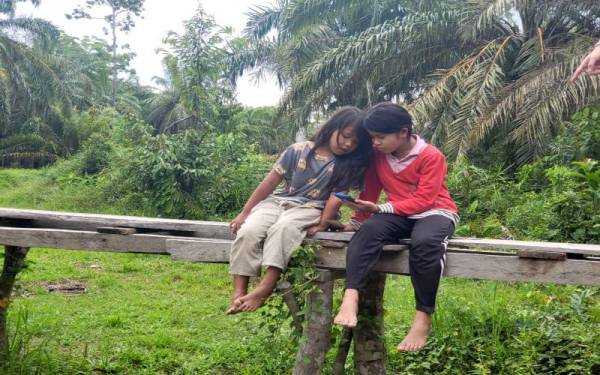 Mazlieyana (kanan) bersama sepupunya, Nuremly Khairul Azwan, 8, (kiri) dapat melayari internet di halaman rumah di Kampung Labi selepas WiFi disediakan di rumah mereka.