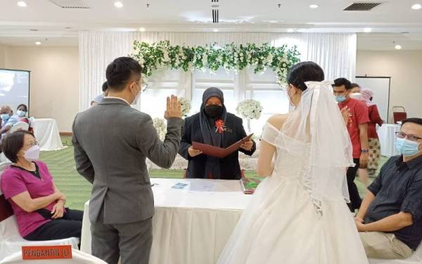 Heng Guan Sen (dua kiri) ketika mendaftarkan perkahwinannya di JPN Melaka, di Ayer Keroh pada Selasa.