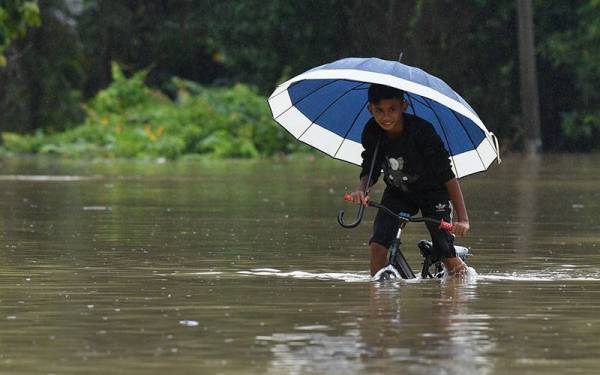 Seorang kanak-kanak berbasikal di jalan yang ditenggelami banjir semasa tinjauan di Kampung Teladas di sini hari ini.