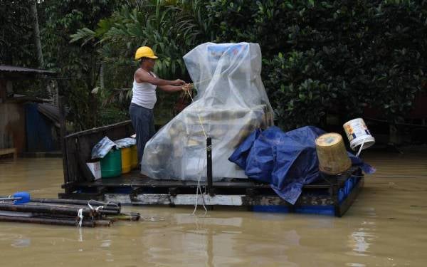 Tarmizi menyarung plastik pada barangan perniagaan gerainya yang diletakkan di atas rakit ekoran Kampung Teladas, Kemaman dilanda banjir. - Foto Bernama