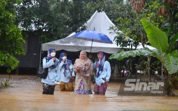 Zaleha (dua, dari kanan) terpaksa mengharungi banjir di depan kediamannya untuk menghadiri majlis akad nikah di Masjid Matang, Hulu Terengganu.