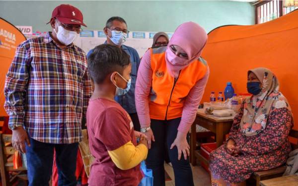 Rina (tengah) menyantuni seorang kanak-kanak yang dipindahkan ke PPS) di Sekolah Kebangsaan Bukit Mentok pada Isnin ekoran rumahnya ditenggelami banjir. - Foto Bernama