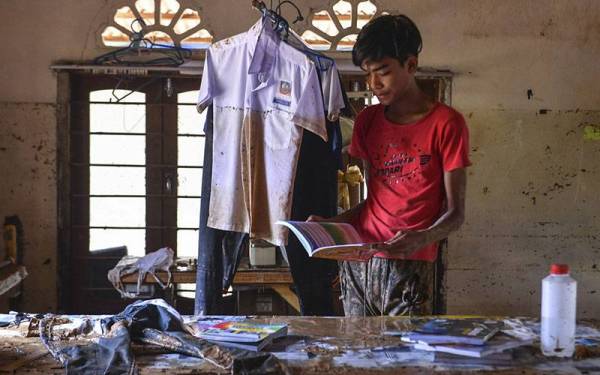 Calon SPM, Mohd Fakhrul Radzi, 18, melihat keadaan baju dan buku sekolah yang diselaputi lumpur selepas rumahnya ditenggelami banjir semasa tinjauan di Kampung Padang Tersat hari ini. - Foto Bernama
