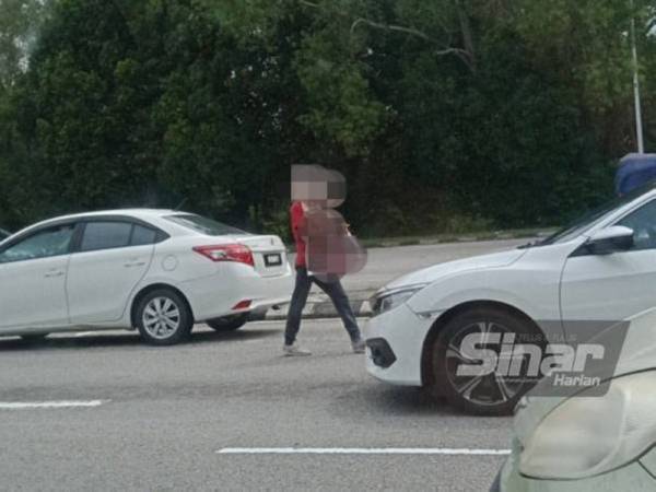 
Penjaja lampu isyarat berjalan di pembahagi jalan sambil membawa makanan untuk dijual kepada pemandu kenderaan sementara menunggu lampu isyarat berubah hijau.