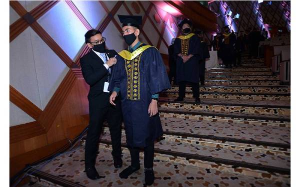 Petugas sedang membetulkan jubah seorang graduan yang sedang menanti giliran untuk
penganugerahan