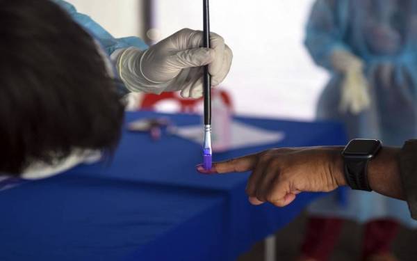 Kakitangan Kementerian Kesihatan Malaysia menyapu dakwat kekal ke jari anggota Angkatan Tentera Malaysia (ATM) yang bergejala, kontak rapat atau positif untuk mereka menunaikan tanggungjawab sebagai pengundi ketika proses undi awal bagi Dewan Undangan Negeri (DUN) N.29 Mahkota sempena Pilihan Raya Negeri (PRN) Johor di Kem Mahkota hari ini.
