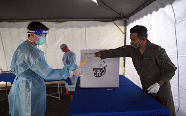 Anggota Angkatan Tentera Malaysia (ATM) yang positif Covid-19 memasukkan kertas undi ke dalam sampul plastik khas yang disediakan sambil dibantu oleh kakitangan Kementerian Kesihatan Malaysia agar mereka menunaikan tanggungjawab sebagai pengundi ketika proses undi awal bagi Dewan Undangan Negeri (DUN) N.29 Mahkota sempena Pilihan Raya Negeri (PRN) Johor di Kem Mahkota hari ini.