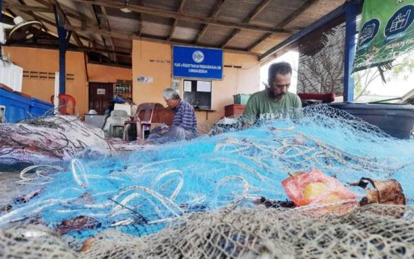 Aziz (kiri) bersama rakannya membaiki pukat yang rosak di jeti nelayan Beserah pada Selasa