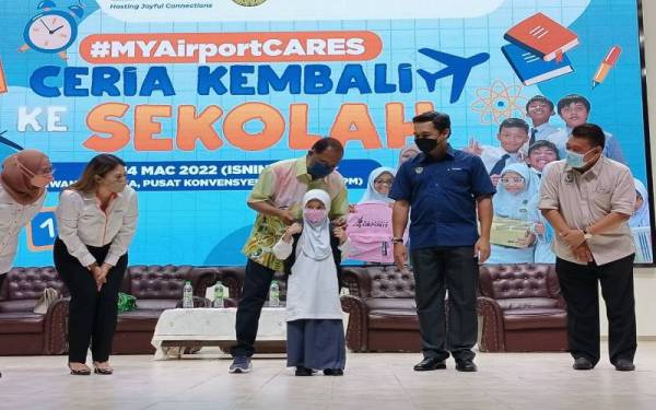 Zambry membantu memakaikan beg kepada seorang penerima sempena Program Ceria Kembali ke Sekolah #MyAirportCARES di Dewan Merdeka Seri Manjung pada Isnin.