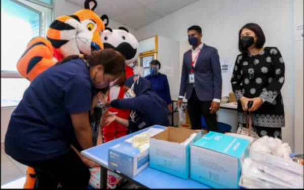 Dua maskot Kellogg menemani seorang kanak-kanak menerima suntikan vaksin di Sehat Healthcare Center, Seremban pada Jumaat. Turut kelihatan Matan Raj (dua dari kanan).