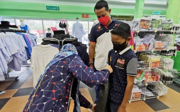 Mohd Fauzi (tengah) melihat isterinya, Roziwati Saad (kiri) mencuba seluar sekolah baharu untuk anaknya.