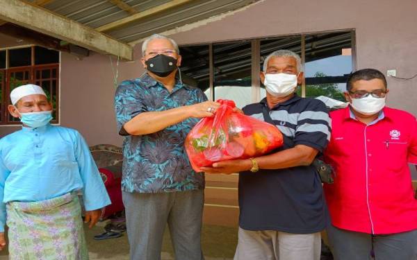 Annuar (dua, kiri) menyampaikan sumbangan kepada mangsa banjir di Kampung Serongga, Repek, Pasir Mas pada Isnin.