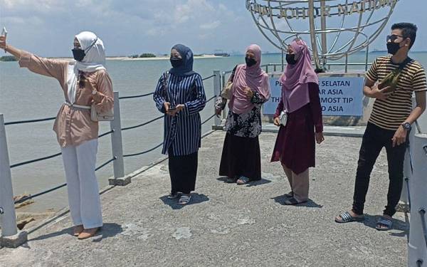 Badrul Amin (kanan) bersama keluarganya tidak melepaskan detik bergambar ketika bayang mereka semakin mengecil ketika fenomena tanpa bayang di Taman Negara Johor Tanjung Piai pada Khamis.