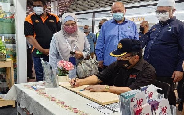 Ahmad menandatangani buku lawatan sambil diperhatikan Razman (kanan) ketika mengunjungi booth Jabatan Perikanan Perak.