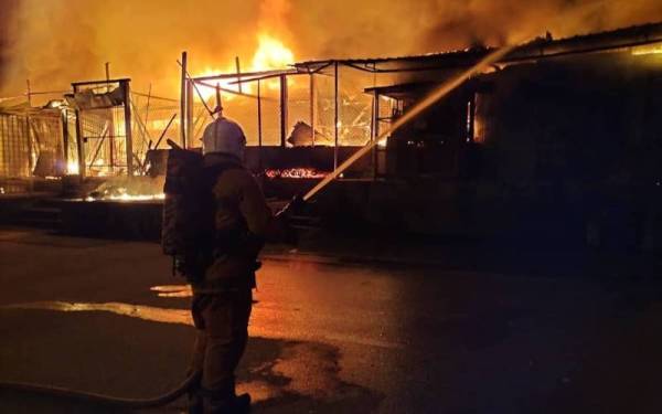 Anggota bomba memadamkan kebakaran melibatkan 15 lot kedai yang musnah sehingga 95 peratus.