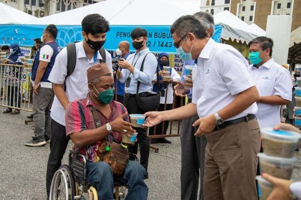 Burhanuddin Hilmi (kanan) mengagihkan bubur lambuk kepada orang ramai di hadapan Masjid Abidin pada Ahad.