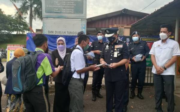 Razali (tiga dari kiri) mengedarkan buku nota kepada pelajar ketika program 1st Day At School di SMK Durian Tunggal, di sini, pada Selasa.
