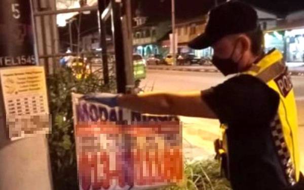 Anggota polis menurunkan poster poster tawaran pinjaman wang tidak berlesen yang ditampal di bandar ini.