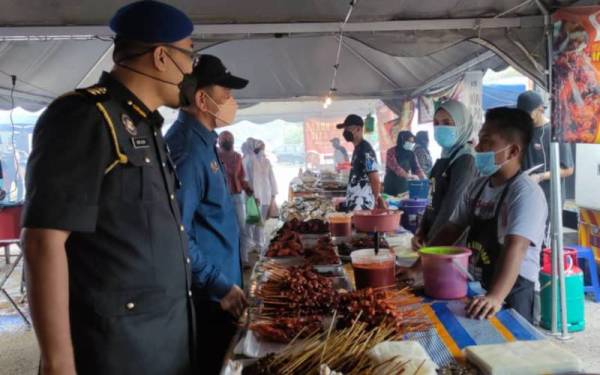 Saharuddin (dua, kiri) bertanya mengenai harga dan bekalan ayam segar kepada peniaga ayam bakar di bazar Ramadan Batu Burok, pada Khamis.