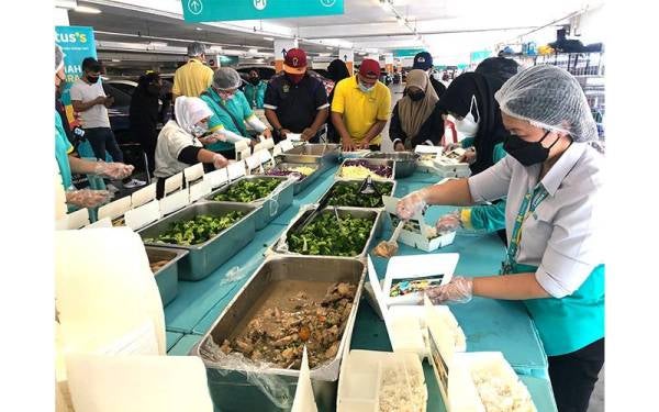 Siuew Luan (kanan) dan sukarelawan Food Aid Foundation serta kakitangan Lotus’s mengisi makanan ke dalam kotak sebelum diagihkan. 