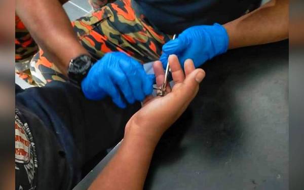 Anggota bomba berusaha memotong cincin besi yang tersangkut pada jari manis tangan kanan seorang remaja lelaki - Foto: ihsan bomba