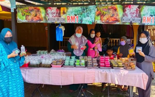 Siti Maimunah (dua dari kiri) menjual kuih-muih pada harga RM1 sepeket bagi membantu meringankan beban penduduk setempat yang dilihat masih lagi terkesan dengan serangan Covid-19 sejak dua tahun lalu.