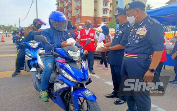Shafien (kanan) mengagihkan bubur lambuk kepada pengguna jalan raya di hadapan IPD Kota Bharu.