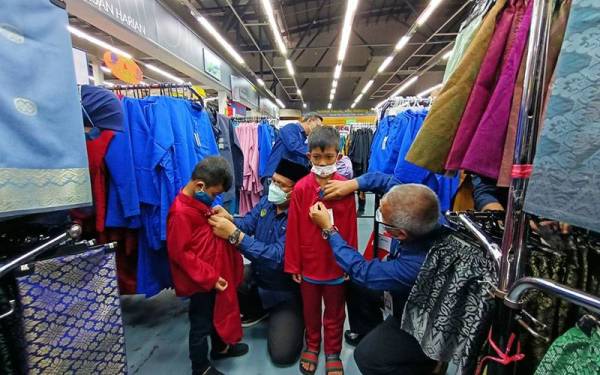 Mohd Akmal (kiri) dan Rosli menyantuni pasangan adik-beradik, Adam Haikal Syayakin, 11, dan Adam Danial, 9, mencuba baju raya baharu sempena Program Santuni Asnaf dan Kumpulan Sasar Ramadan anjuran Jabatan Alam Sekitar (JAS) di Pasaraya Mydin pada Sabtu.