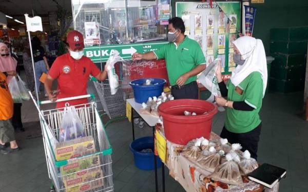 Mas Imran (tengah) mengagihkan bubur lambuk ayam dan daging secara percuma kepada pelanggan di Pasar Raya Econsave Taman Scientex, Pasir Gudang, pada Sabtu