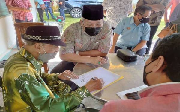 Annuar (tengah) melihat Mat Sentol menulis khat ketika menziarahi seniman veteran itu di kediamannya di Larkin, Johor Bahru, pada Ahad.
