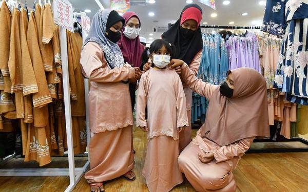 Nor Balqis Batrisya (kanan) dan adik-adiknya mencuba pakaian yang disumbangkan dalam Program Kasih Ramadan Eastern Pacific Industrial Corporation Berhad (EPIC) di sini pada Khamis.