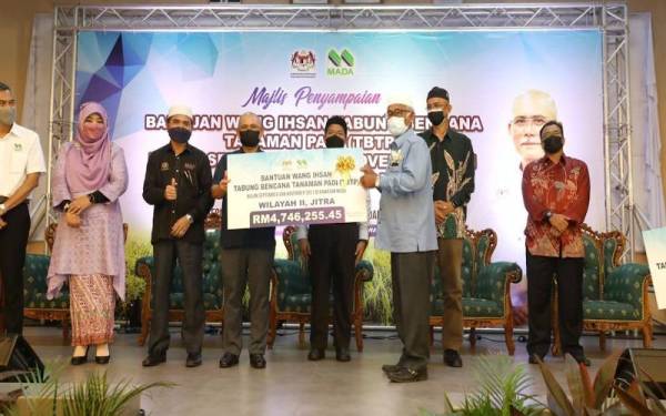 Ronald (empat dari kiri) menyerahkan replika cek kepada wakil pesawah Wilayah II Jitra yang terjejas akibat bencana pada tahun lalu.