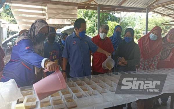 Ahmad (tiga dari kiri) menuang bubur manis ke dalam bekas plastik anjuran Pusat Daerah Mengundi (PDM) Parit Keroma pada Sabtu.