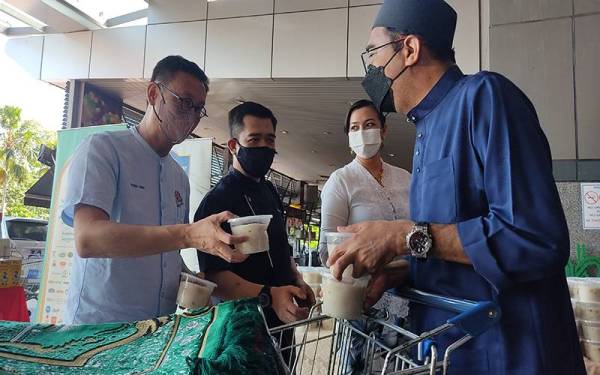 Wong Chen (kiri) bersama Jessica (dua dari kanan) mengedarkan bubur lambuk kepada pengunjung Mydin USJ di Subang Jaya pada Sabtu.