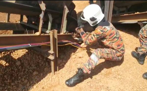 Anggota bomba sedang melonggarkan belting mesin pemecah batu untuk mengeluarkan tangan mangsa yang tersepit. - Foto Ihsan Bomba Pahang